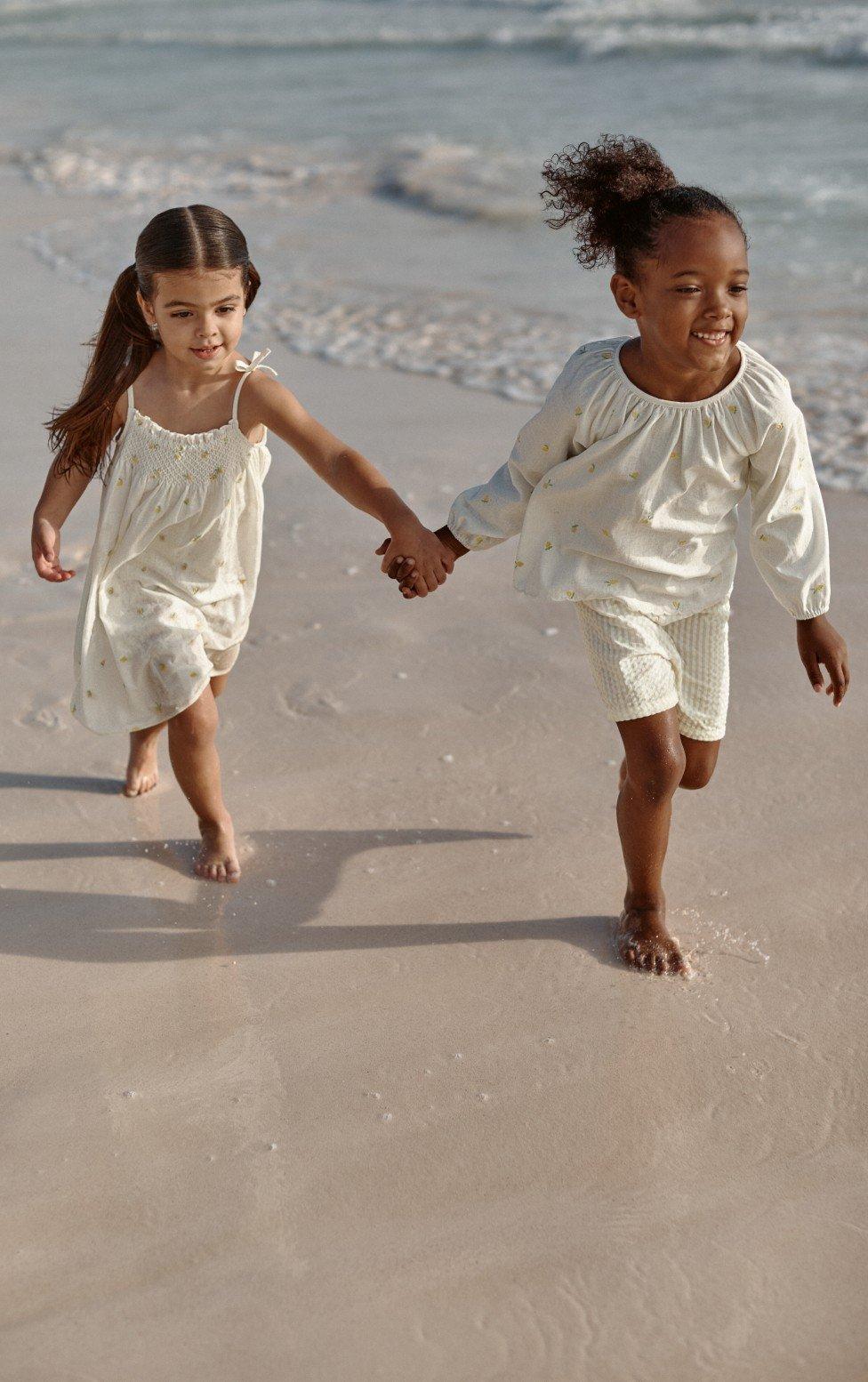 two little girls holding hands as they run along the beach