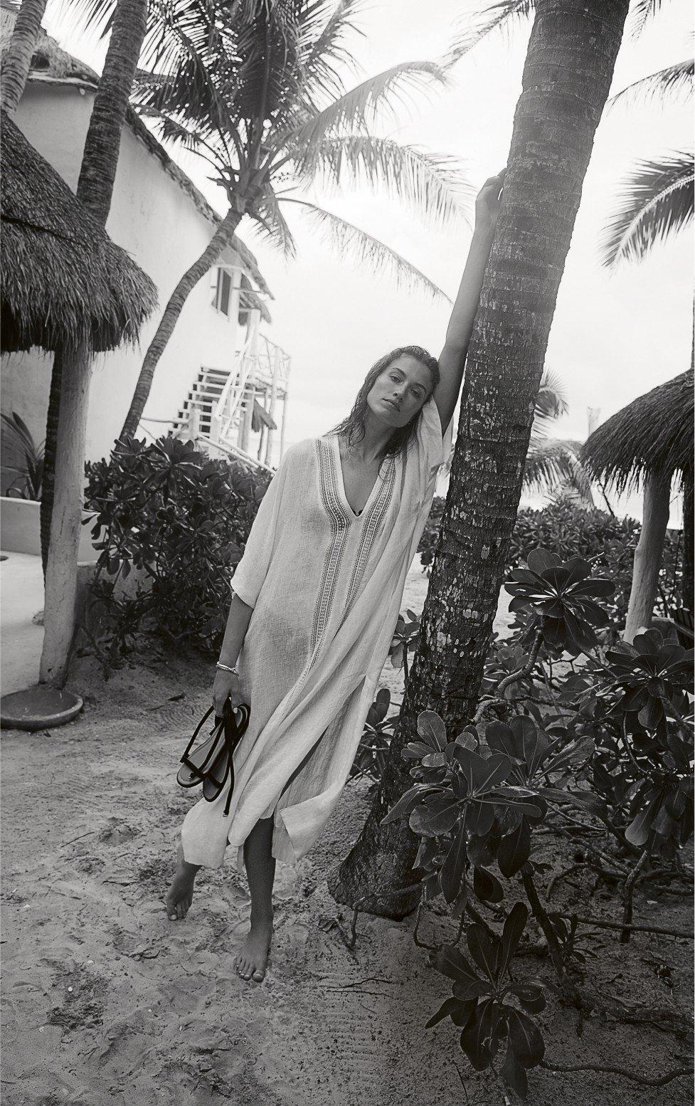a woman in a dress leaning on a palm tree