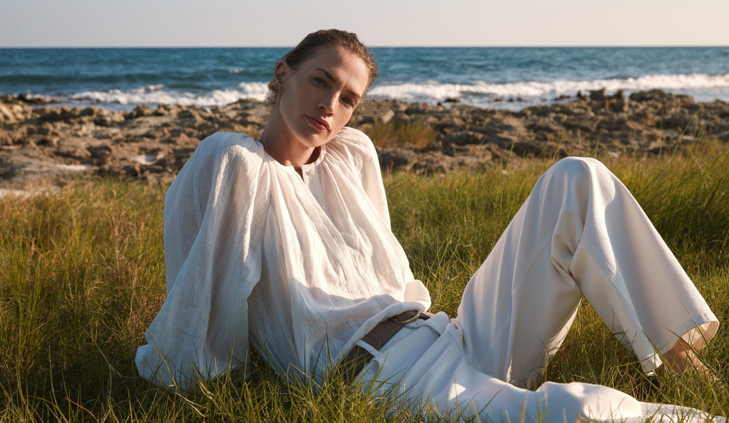 a woman in white sitting on grass near the ocean