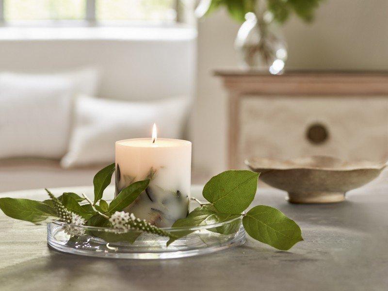 a candle with a small plant on a table next to a vase
