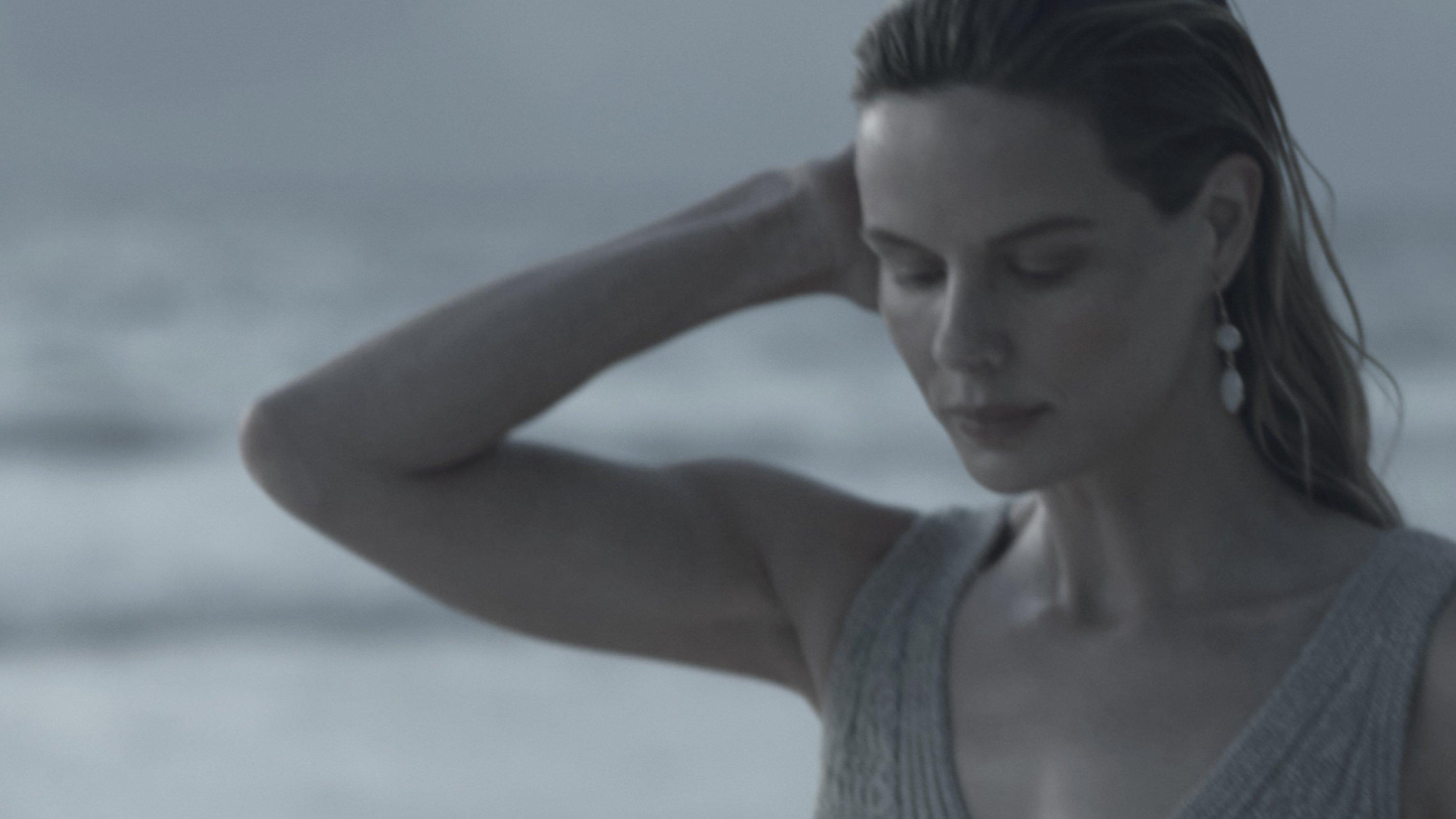 a woman in a grey top standing by the ocean