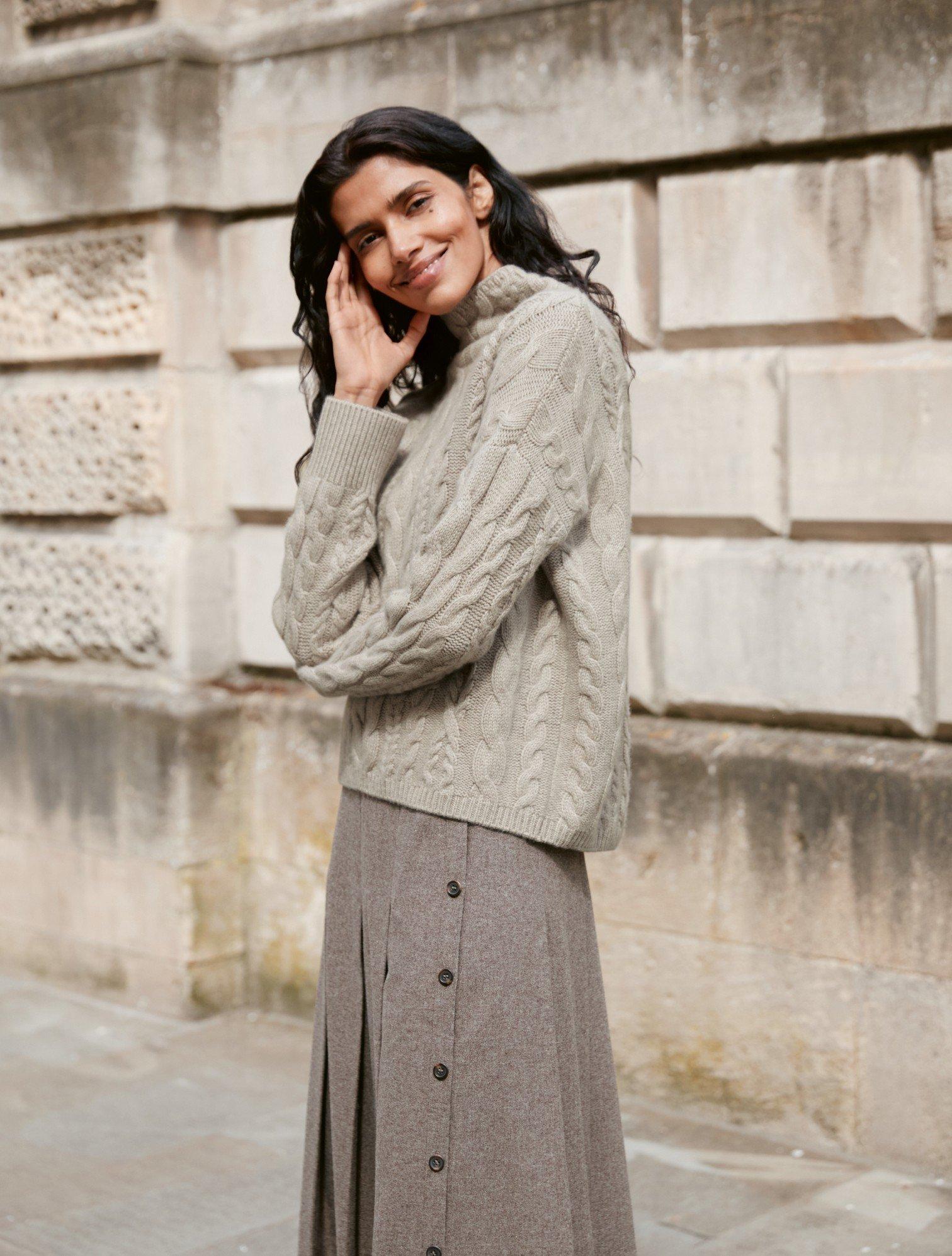 a woman in a gray sweater and skirt standing on a sidewalk