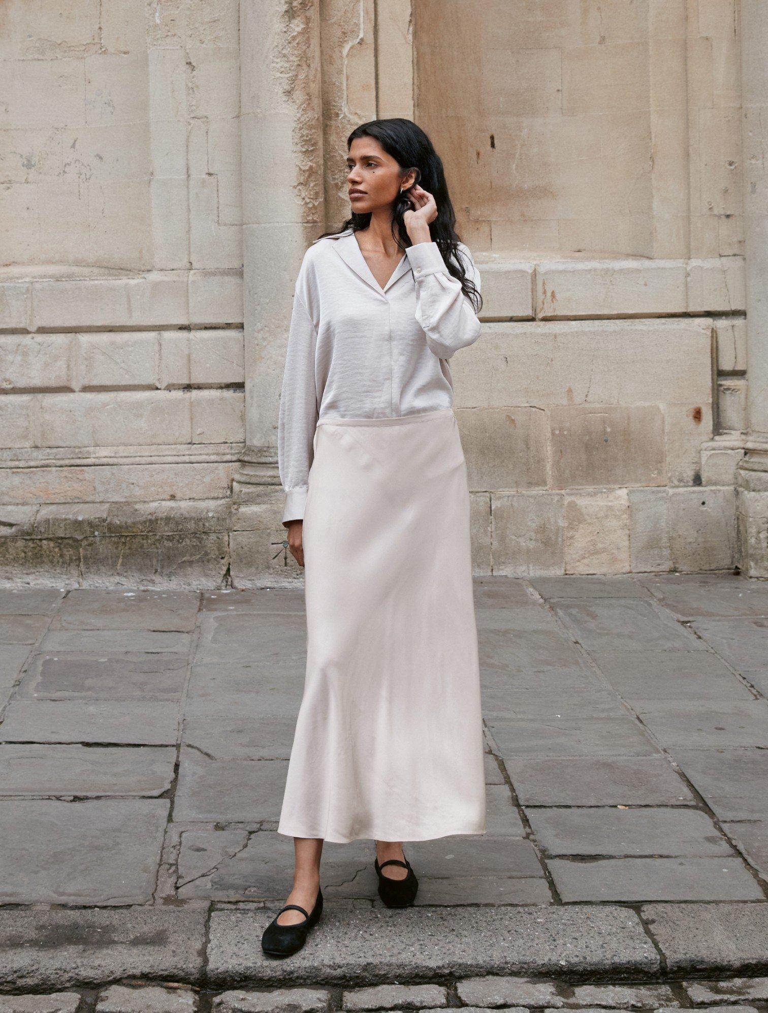 a woman in a white skirt and black shoes standing on a street corner