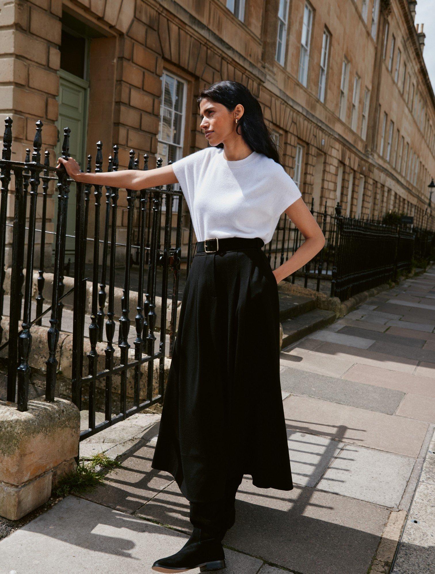 a woman in a white shirt and black skirt leaning against a fence