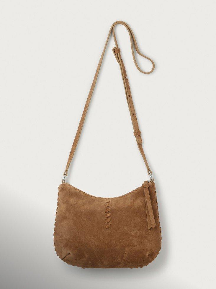 the brown sued crossbody bag hangs from a white wall