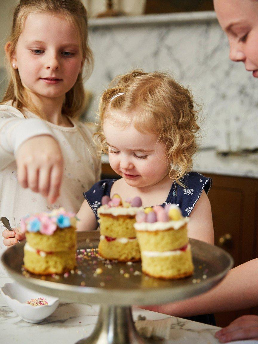 a group of three young girls are helping to decorate a cake