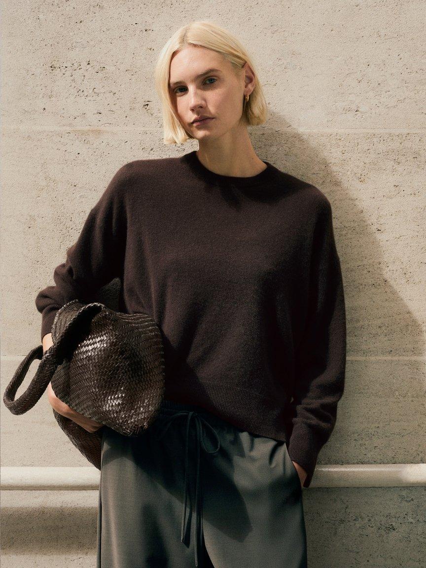 a woman walking down a street in a beige sweater and pants