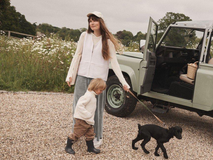 a woman and child walking a dog in a field near a vehicle