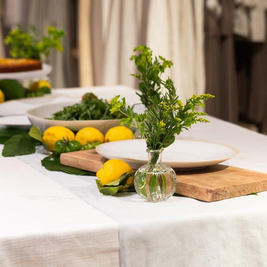 a table with a vase of lemons and a plate of greens