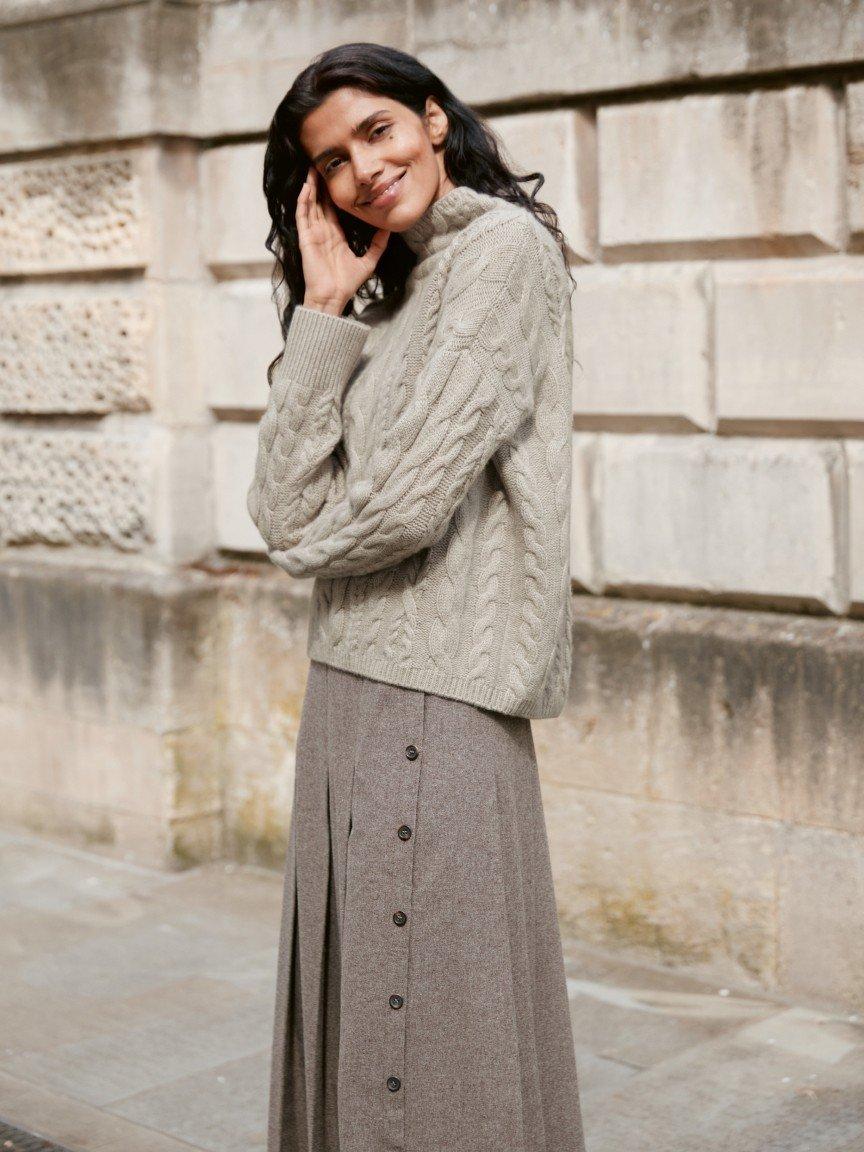 a woman in a brown coat standing in front of a wall