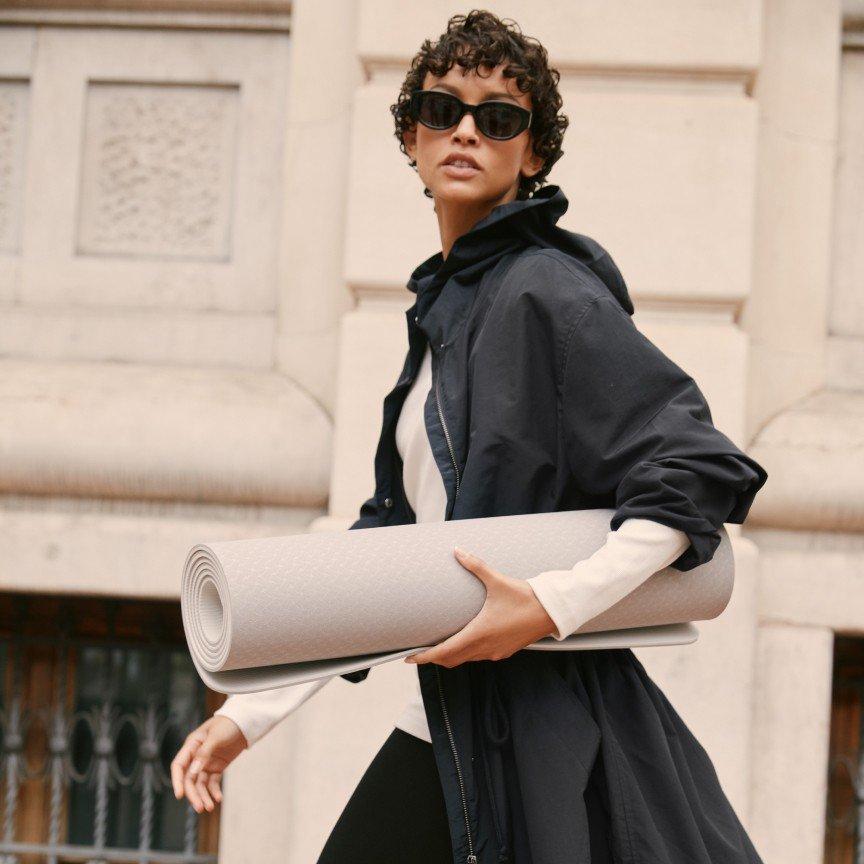 a woman in sunglasses holding a yoga mat on a city street