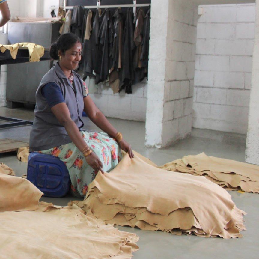 a woman sitting on floor in a factory cutting up leather