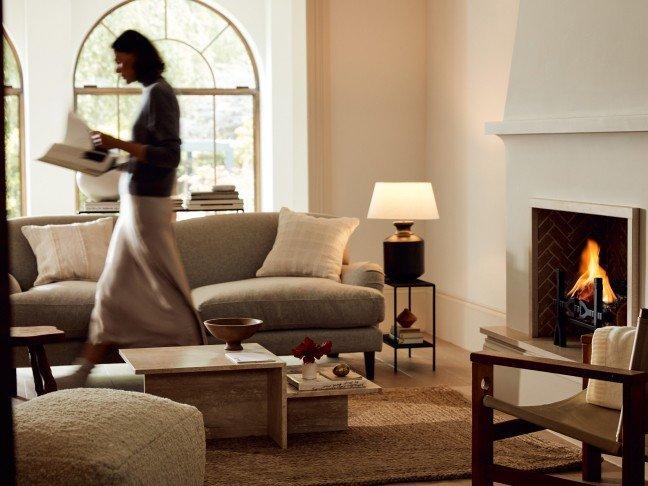 a woman walking through a living room with a fireplace and couches