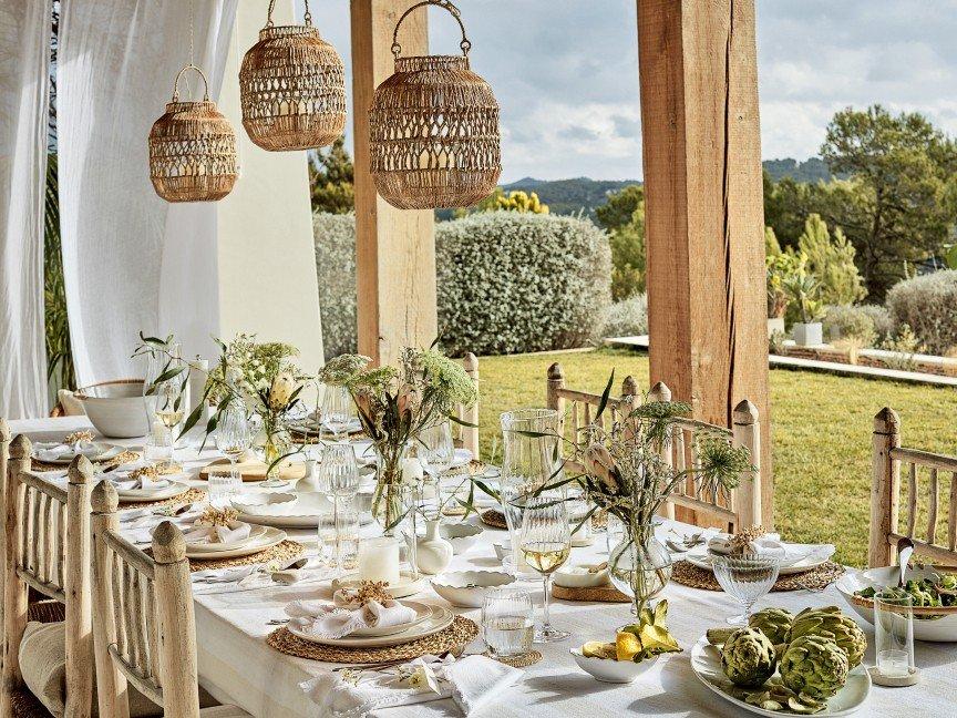 a table set with white plates and white napkins on a covered porch