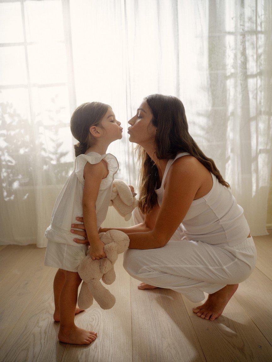 a woman kissing a little girl on the cheek while holding a teddy bear