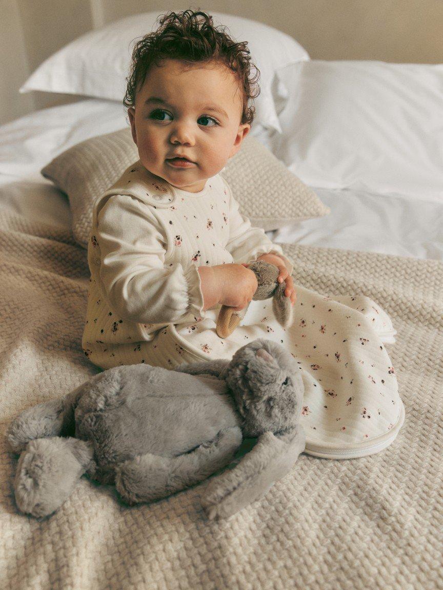 a baby sitting on a bed with a stuffed animal