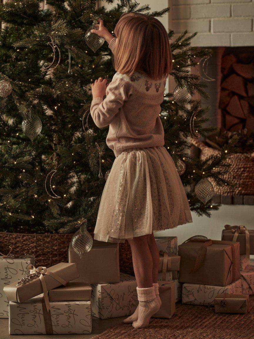 a little girl in a dress decorating a christmas tree