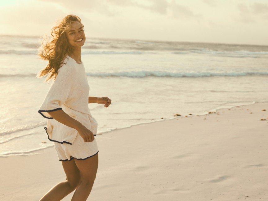 a woman running on the beach with a white shirt and shorts