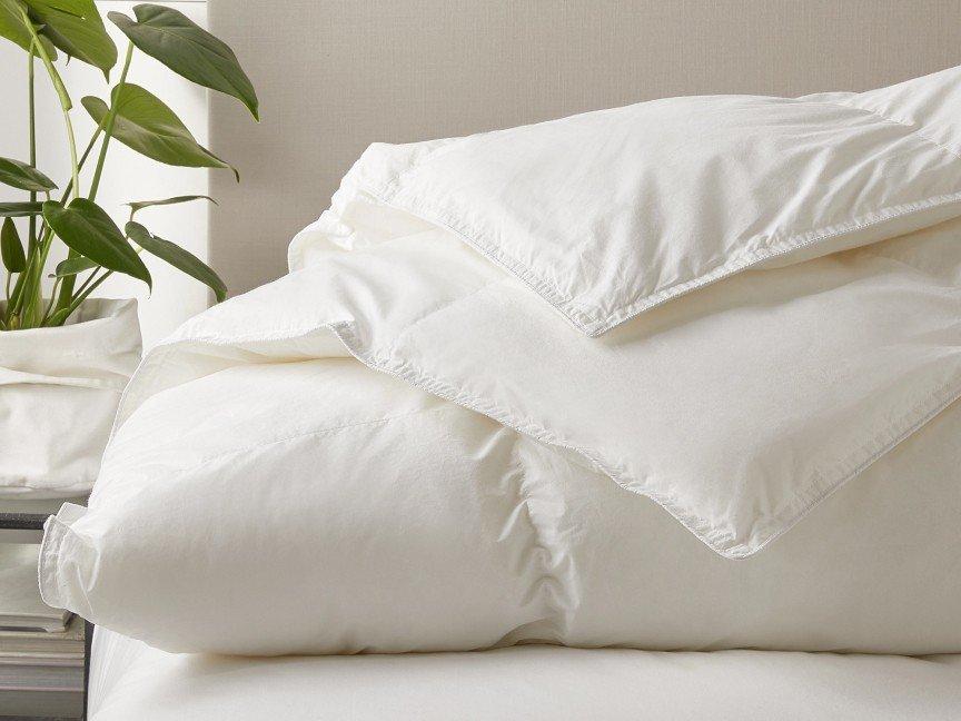 a bed with a white comforter and a plant on top of it