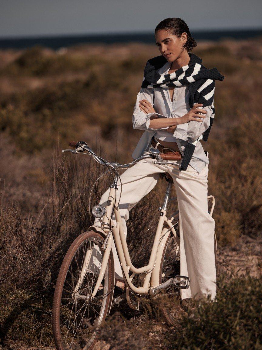 a woman in a white shirt and pants leaning on a bicycle