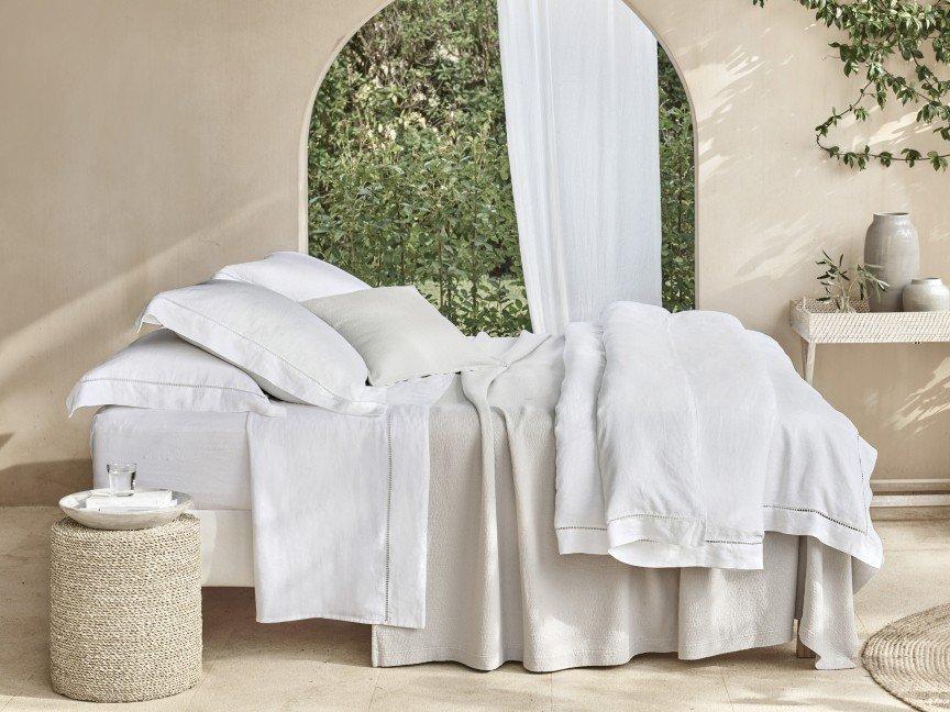 a bed with white sheets and pillows in a room with a window