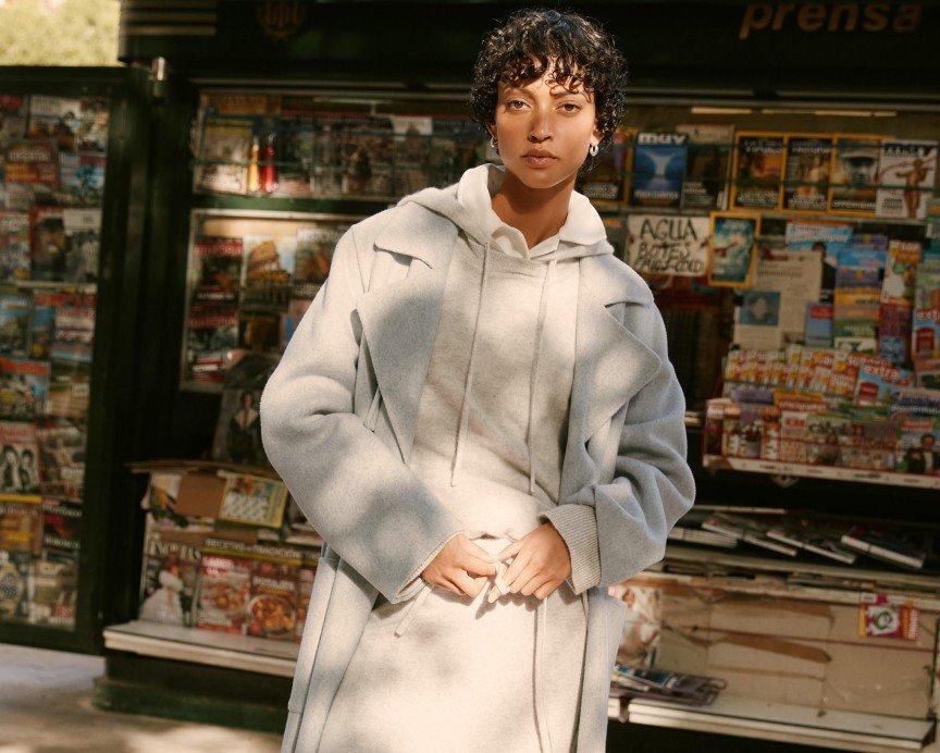 a woman in a white coat standing in front of a store