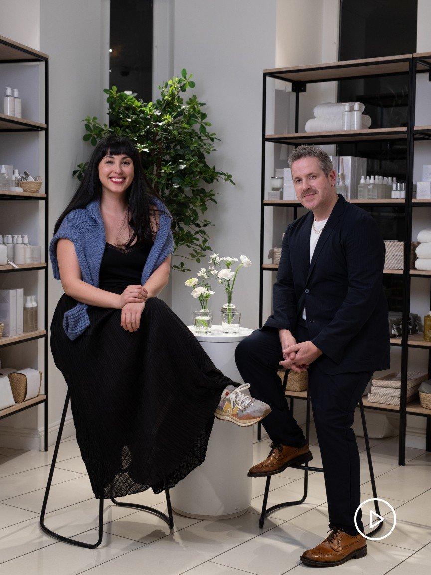 a man and woman sitting on stools in a store room