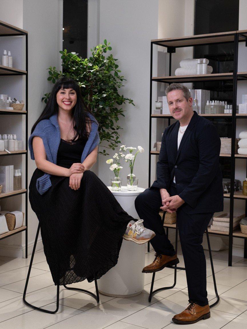 a man and woman sitting on stools in a store room
