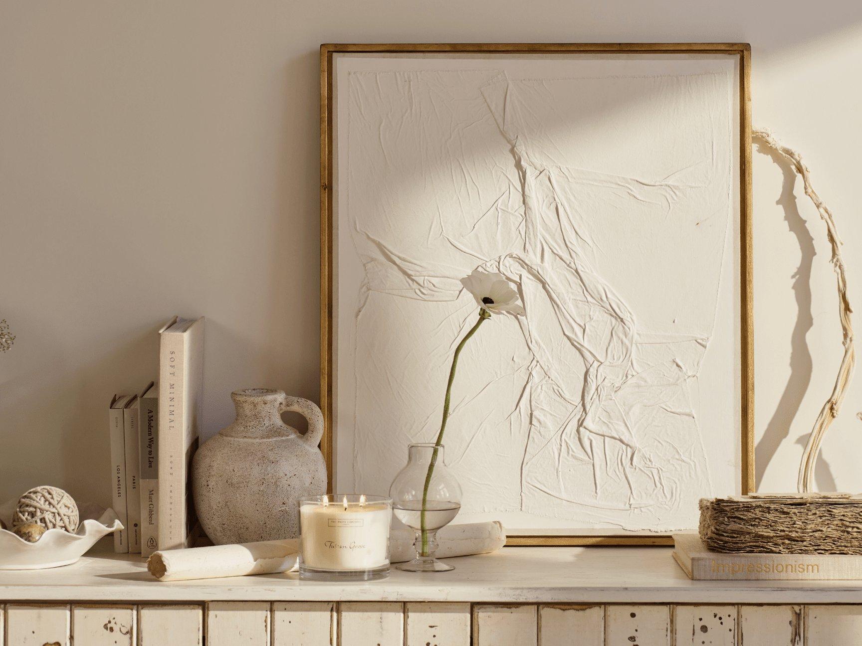 a white vase with a single flower on a shelf next to a painting