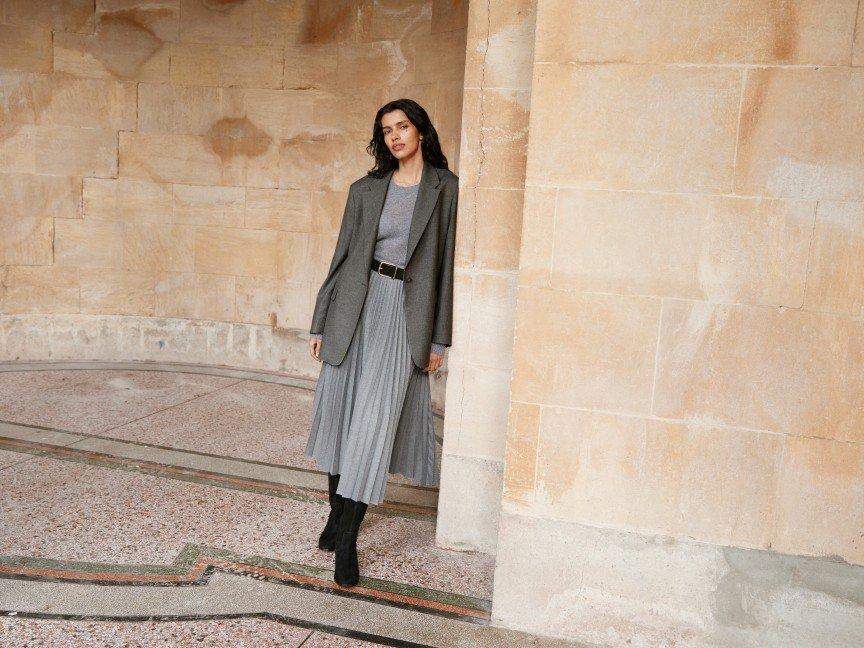 a woman in a gray dress and black boots standing in a hallway