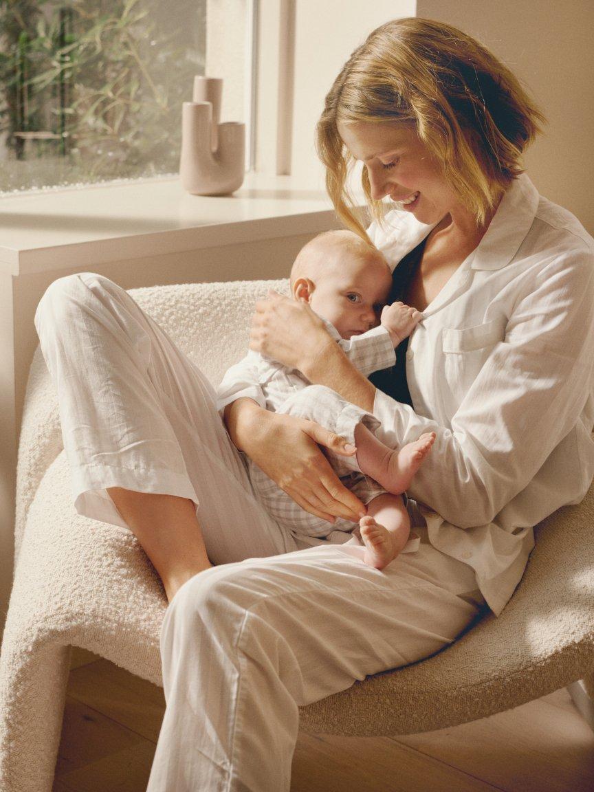 a woman in white pajamas holding a baby in a chair