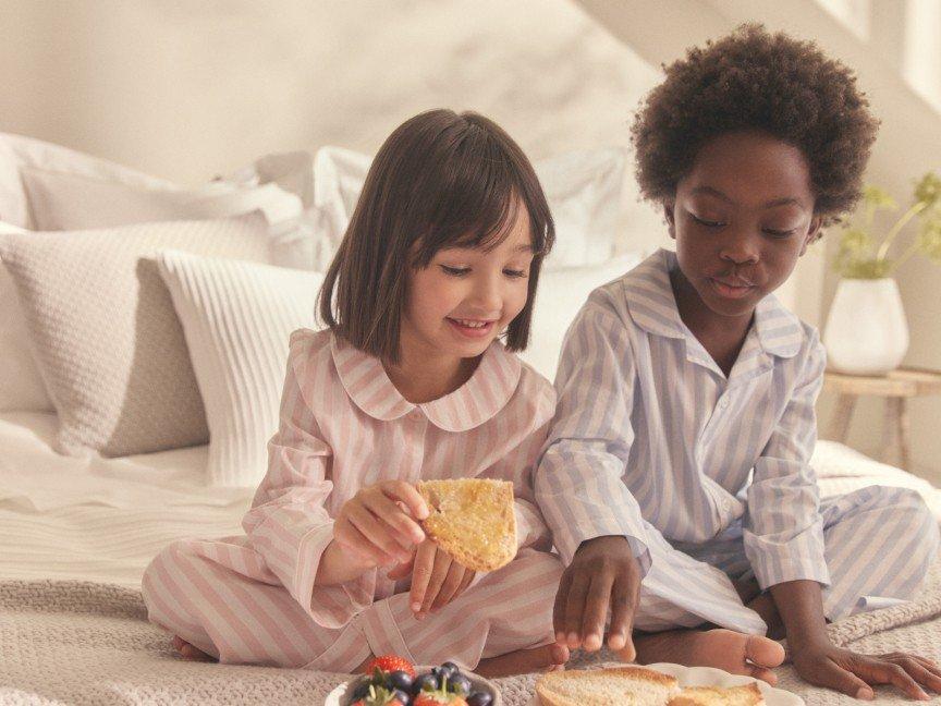 two children sitting on a bed eating food together