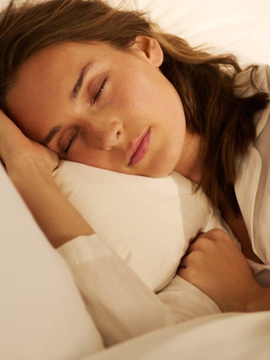 a woman sleeping in bed with her eyes closed and her head resting on the pillow