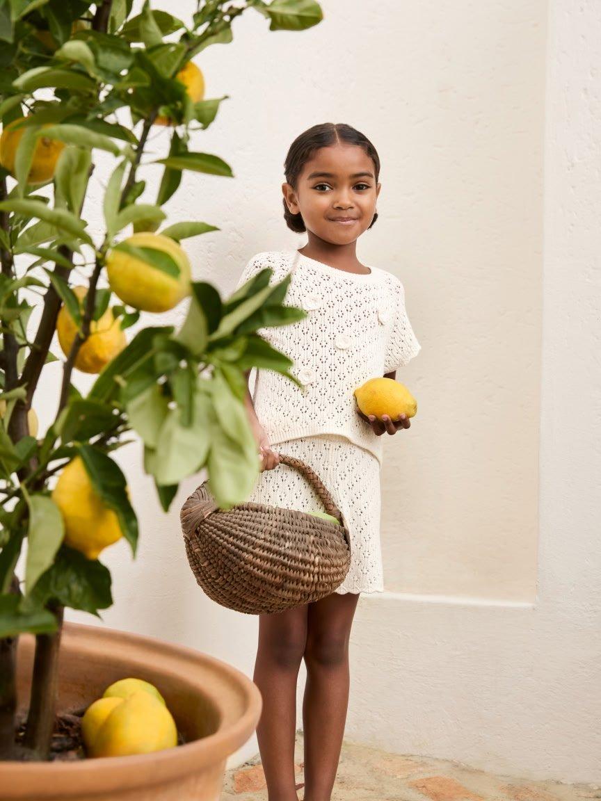 a young girl holding a basket of lemons and a potted plant
