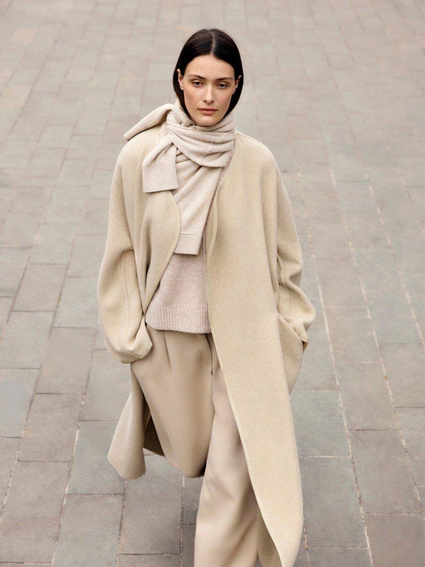 a woman in a beige coat walking down a brick walkway