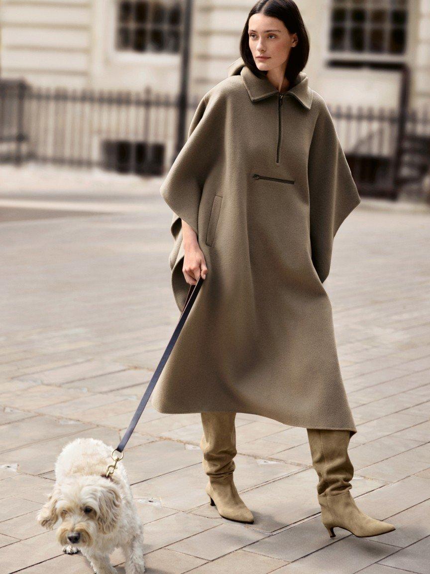 a woman in a beige coat walking down a brick walkway