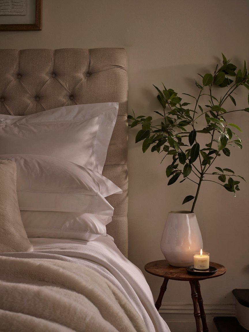 a bed with a candle on a table next to a plant