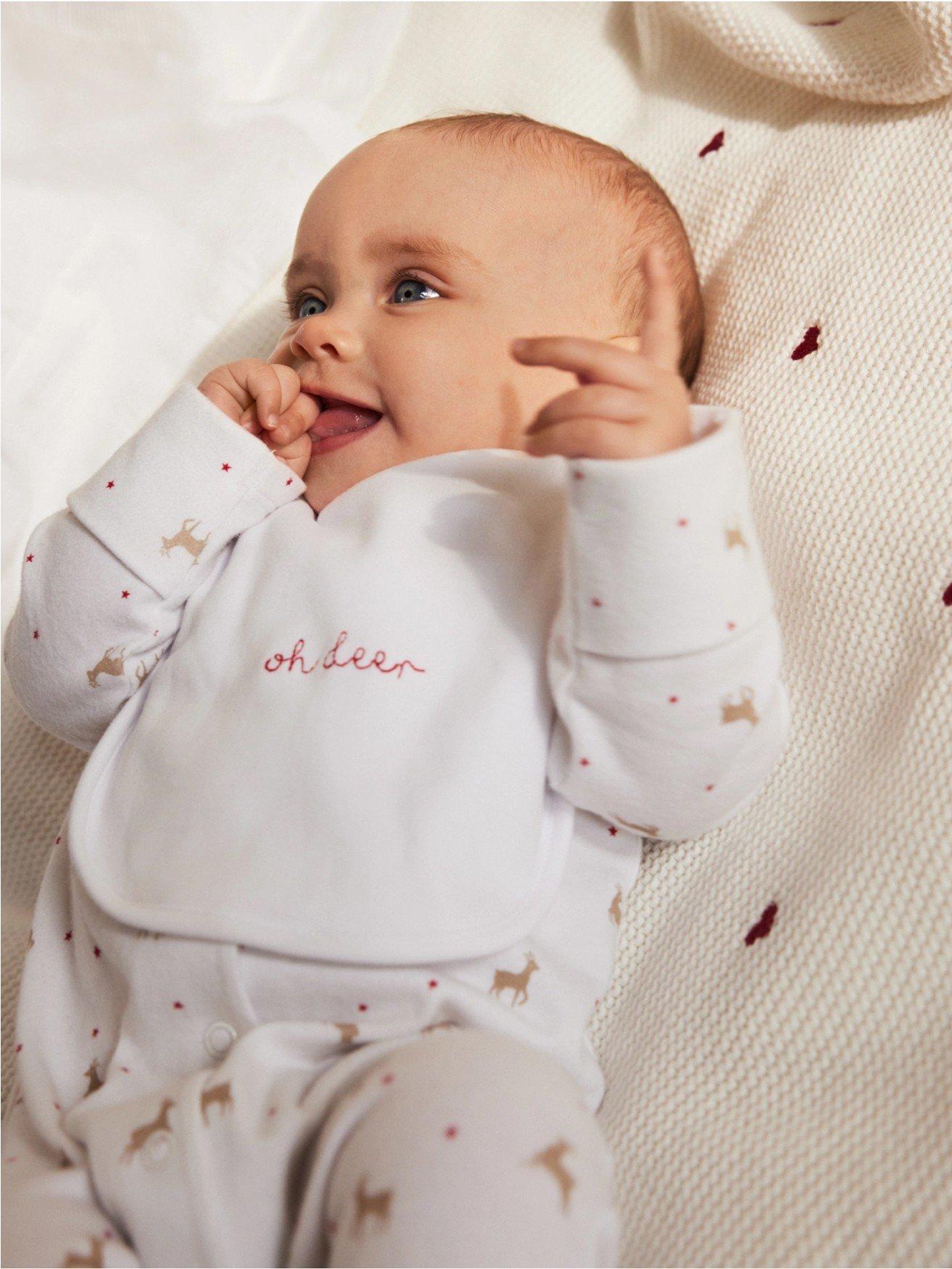 a baby laying on a bed with a white outfit on