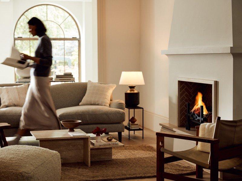 a woman walking through a living room with a fireplace