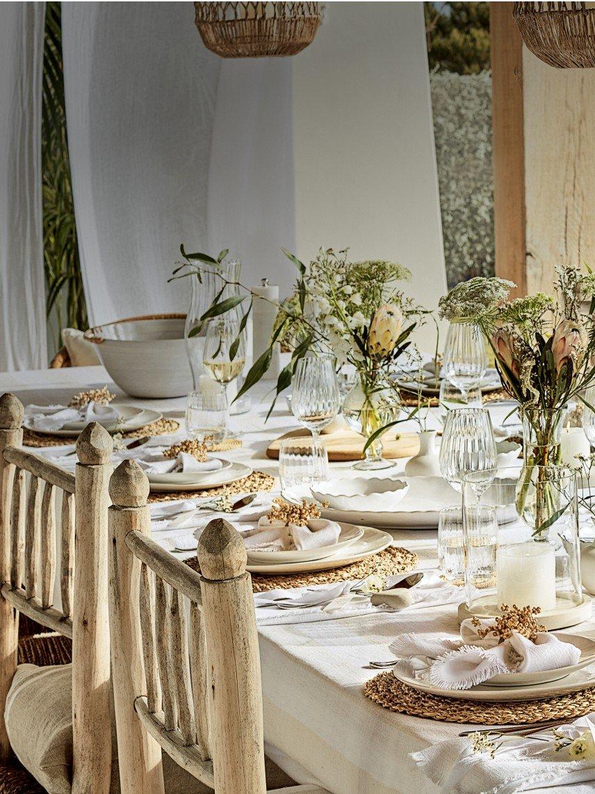 a table set with white plates and white napkins on a patio