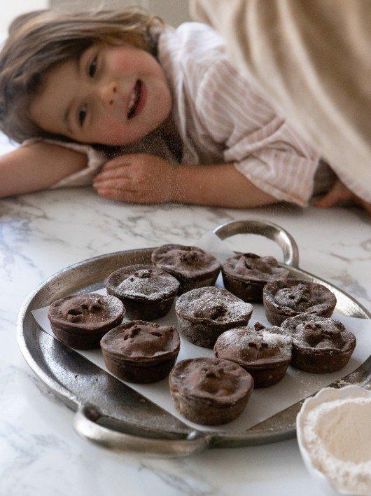 a little girl laying on a table next to a tray of cupcakes