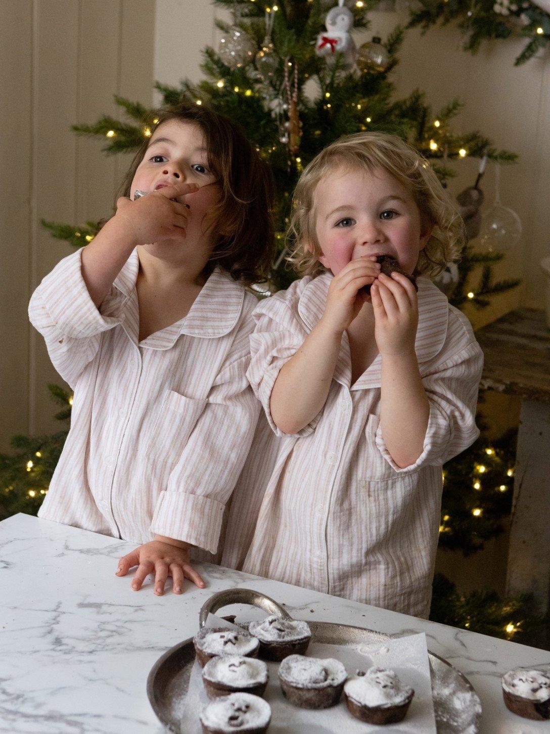 two young girls in pajamas eating pastries in front of a christmas tree