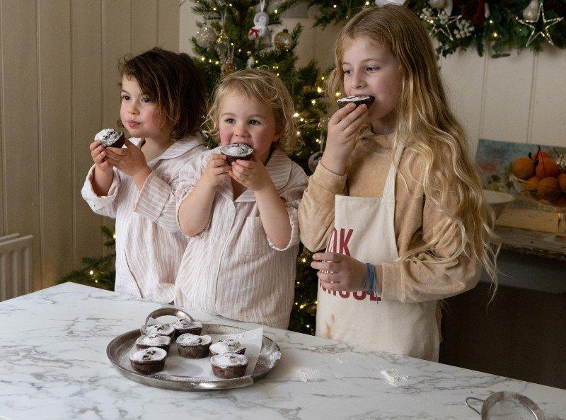 three young girls standing around a table eating cupcakes