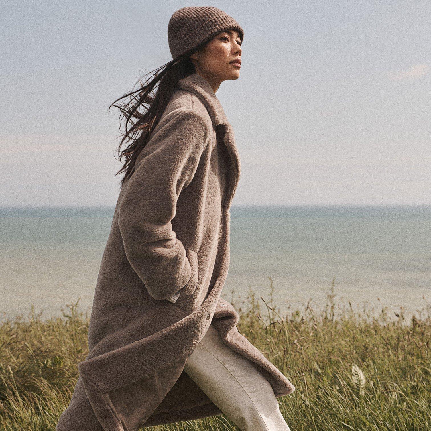 a woman in a hat and coat walking on a beach