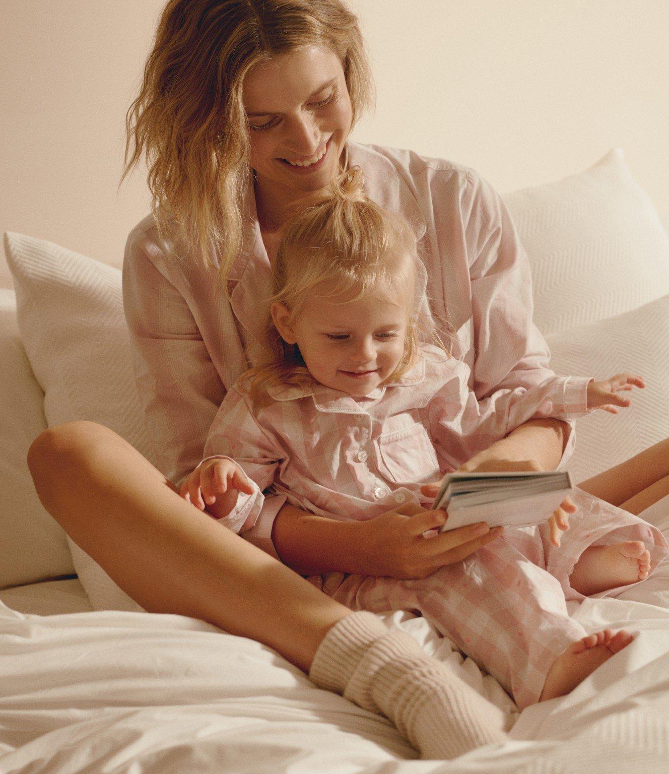 a woman and child sitting on a bed reading a book