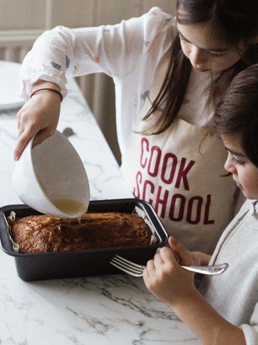 two young girls are pouring milk into a cake in a pan