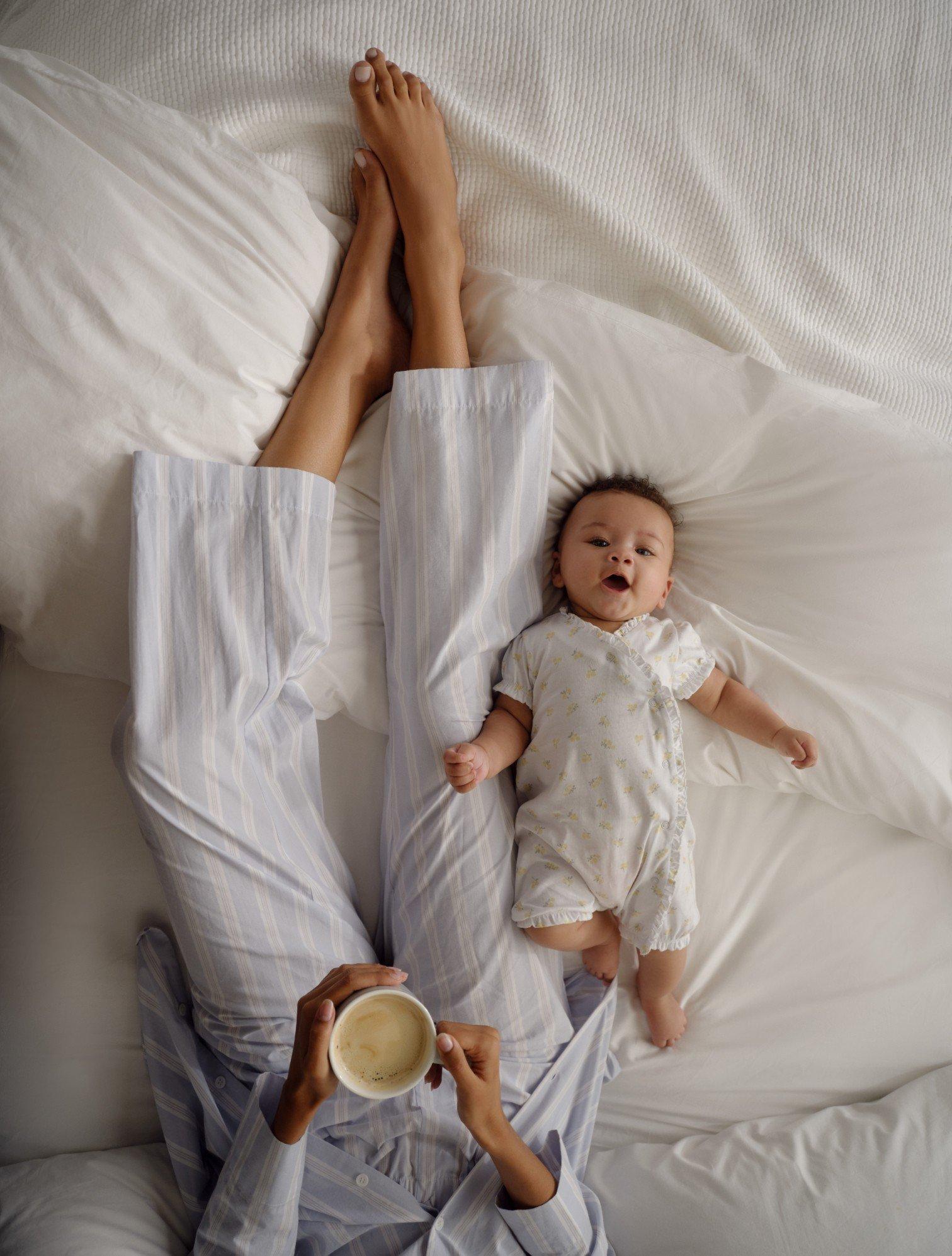 a woman laying in bed holding a cup of coffee and a baby