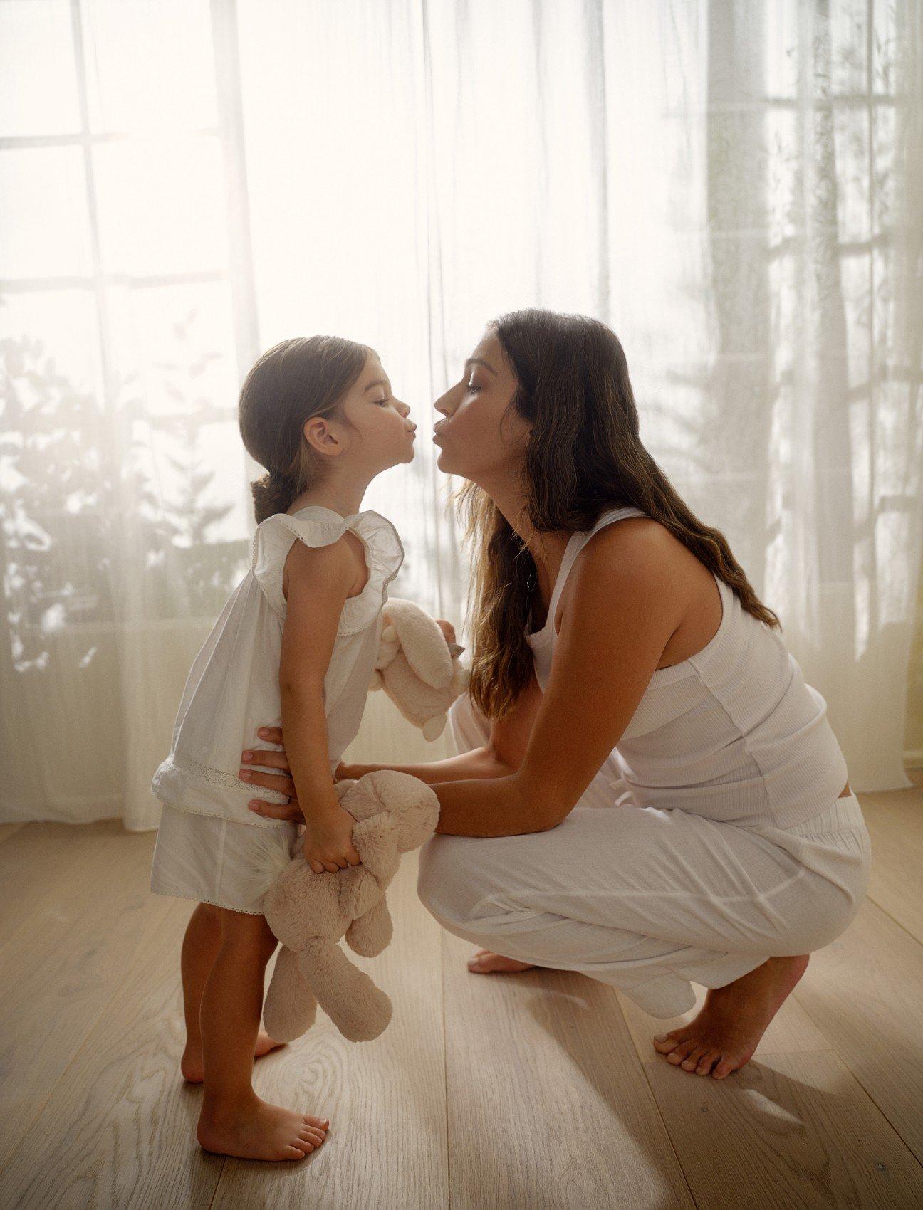 a woman kissing a little girl on the cheek while holding a teddy bear