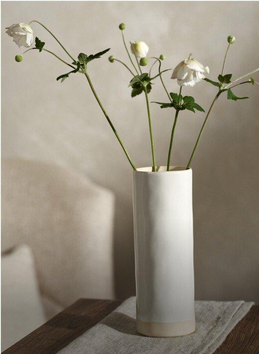 a white vase with flowers on a table in a room