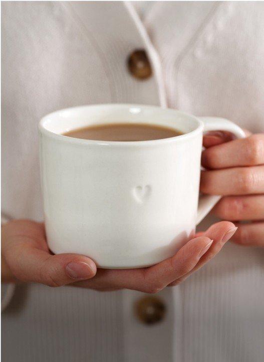 a woman holding a white mug with a heart on it